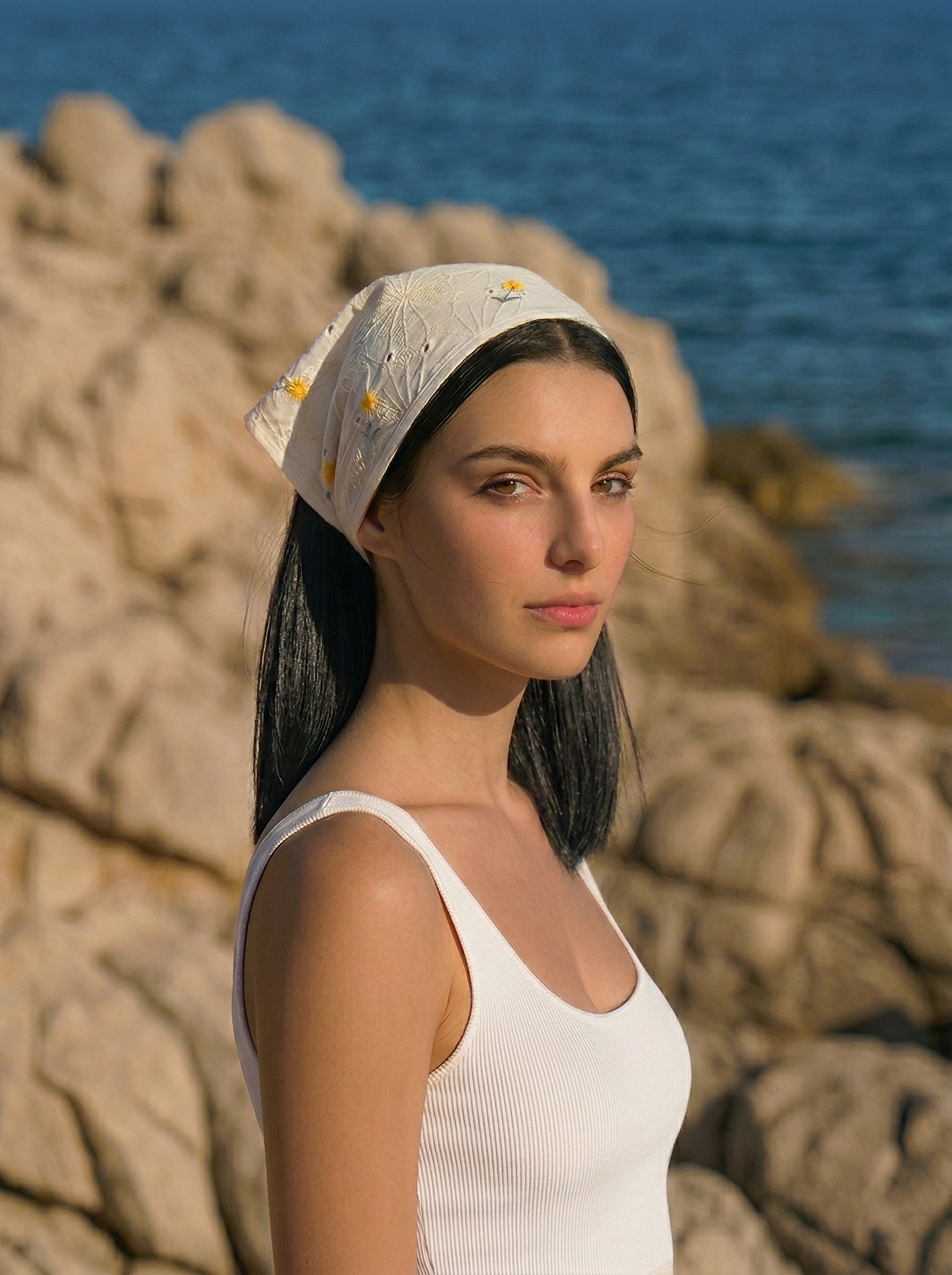 White broderie anglaise bandana with yellow floral embroidery styled as headscarf in beach setting